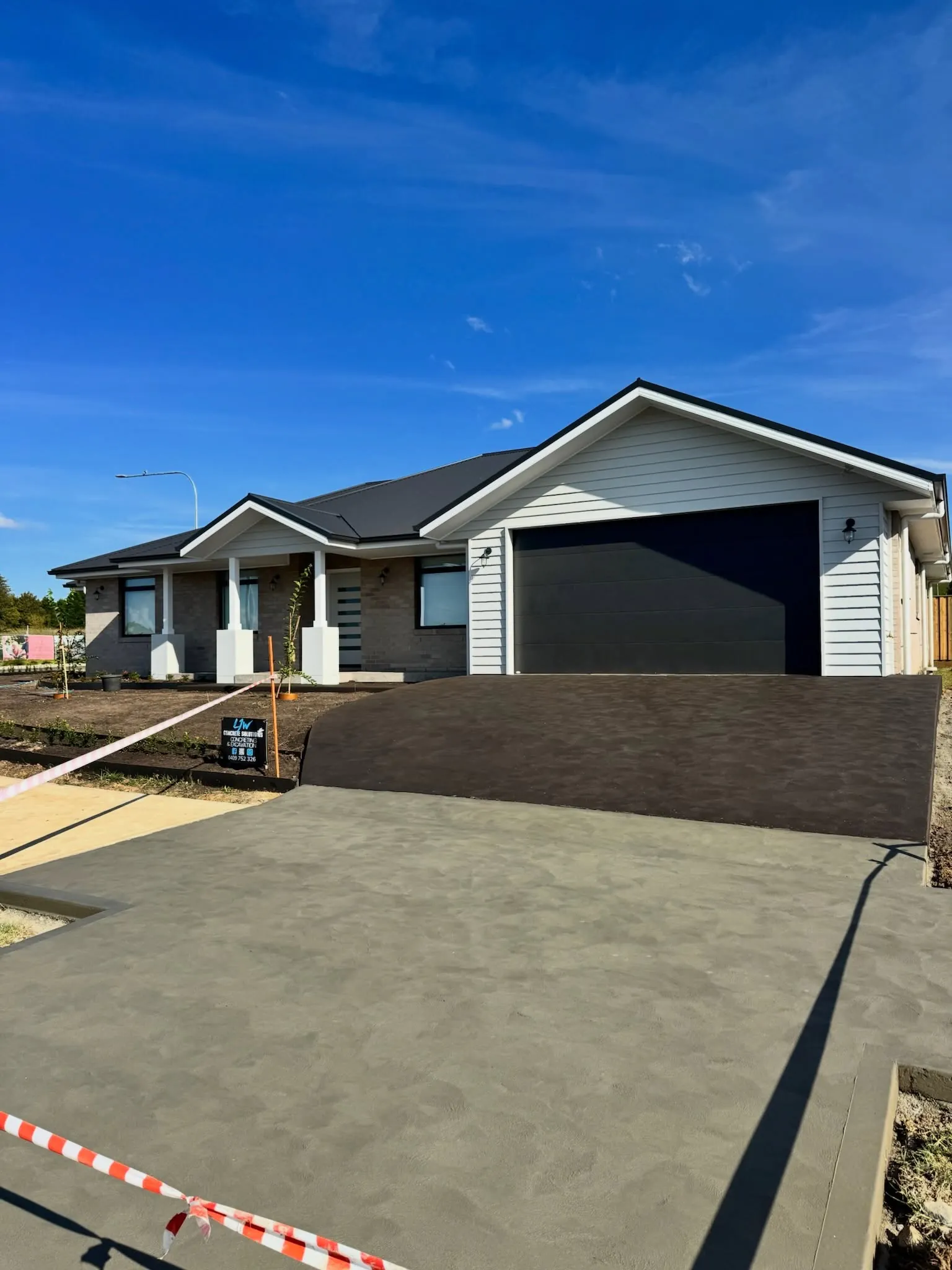 Sealed charcoal concrete driveway with a plain grey crossover, finished by LJW Concrete Solutions