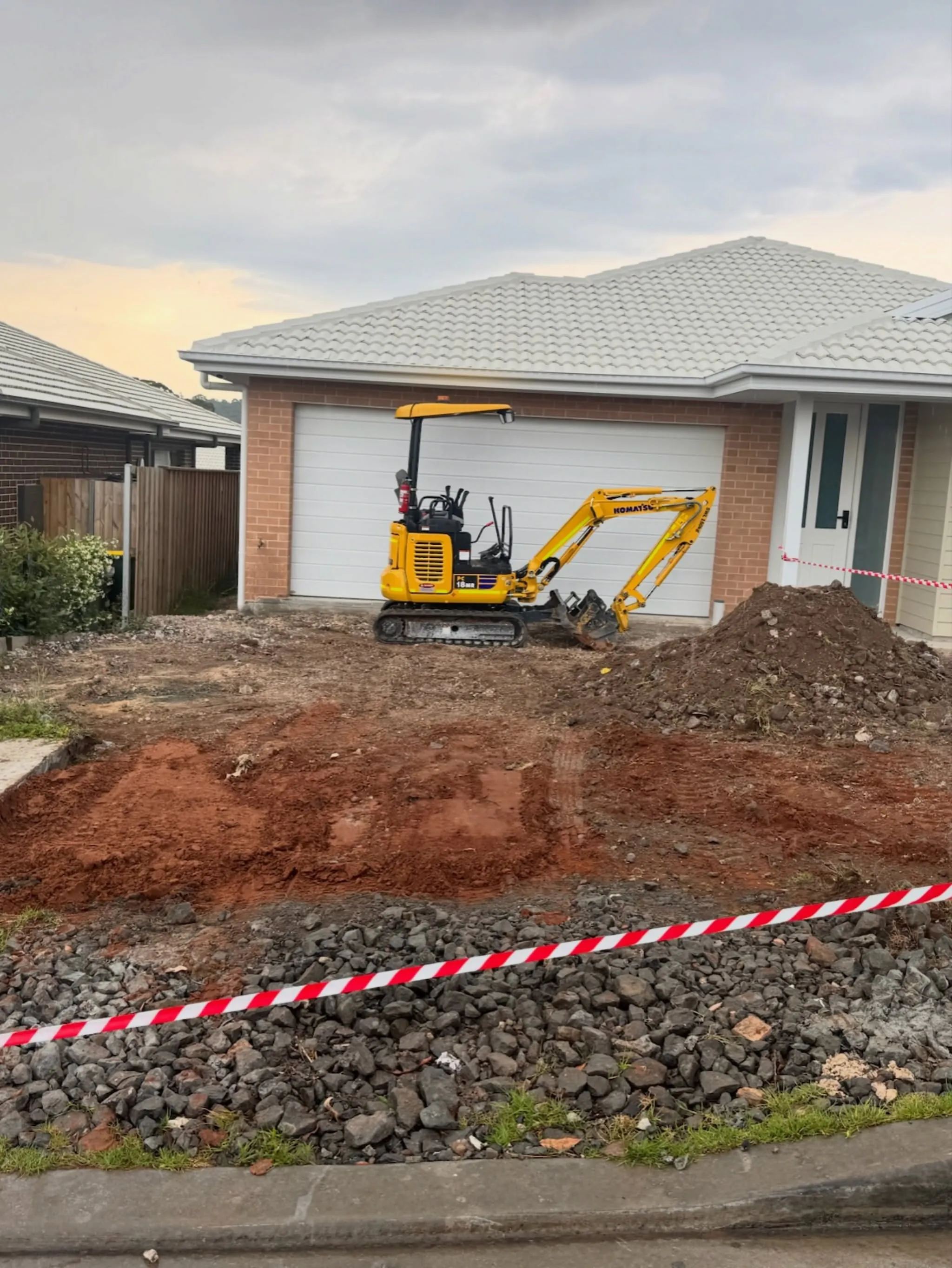 Mini excavator digging out a driveway in front of a new home
